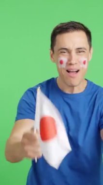 Stüdyoda, Japonya 'yı coşkuyla alkışlayan ve ulusal bayrak sallayan bir adamın krom görüntüsü var.