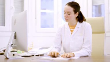 Kadın bir doktorun klinik odasında bilgisayar kullanarak daktilo yazarken yavaş çekim videosu.