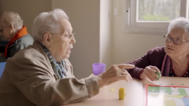 三个老朋友在一个老年病人的游戏中玩着Parcheesi棋盘游戏玩得很开心的慢镜头 — 图库视频影像