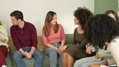Çeşitli etnik çeşitlilikte ve dikkati dağılmış bir grup kadın ve erkeğin bir evde oturup sohbet etmesinin yavaş çekim videosu.