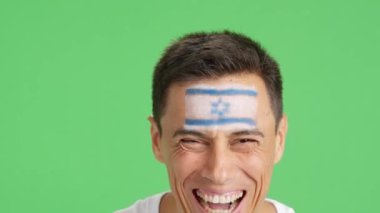 Stüdyoda, yüzünde İsrail bayrağı olan ve kameraya gülümseyen bir adamın krom görüntüsü var.