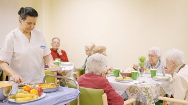 Female cook serving food to a group of seniors in a geriatric clipart