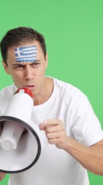 Stüdyoda, yüzünde Yunan bayrağı olan bir adamın megafonla kalabalığı topladığı bir video.