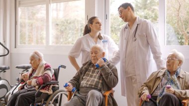 Yaşlı insanlar yaşlılarla egzersiz yaparken dikkati dağılmış iki doktor konuşuyor.