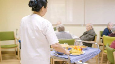 Kadın aşçı yaşlı bir adamın yemek odasına yemekle giriyor.