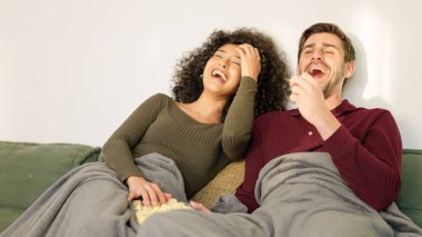 Evde eğlenceli filmler izlerken gülen çok ırklı bir çift.