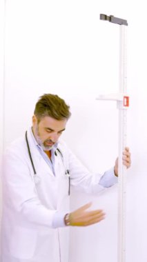 Yetişkin bir erkek doktorun yavaş çekim videosu bir hastadan onu klinikte ölçmek için tartıya çıkmasını istiyor.