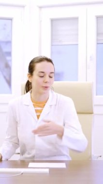 Kadın bir doktorun yavaş çekim videosu hastayı oturmaya davet ediyor.