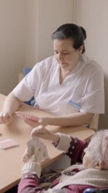 Huzurevinde kart oynayan yaşlı kadın ve bakıcının yüksek görüşlü yavaş çekim videosu