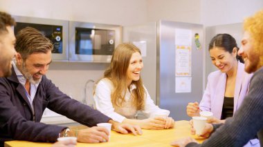 İş arkadaşları ofiste kahve içerken kahkaha atıyorlar.