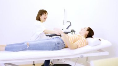 Kadın bir doktorun, bir klinikte sedyede yatan bir hastanın ultrason sırasında hamile olduğunu gösteren yavaş çekim videosu.