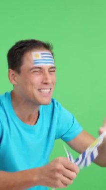 Stüdyoda Uruguay 'a tezahürat eden bir adamın renkli videosu var. Ulusal bir bayrak sallıyor ve boş boş fotokopi odasına bakıyor.