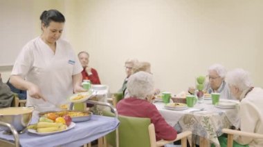 Yaşlı bir gruba yemek servisi yapan bir kadın aşçının yavaş çekim videosu.