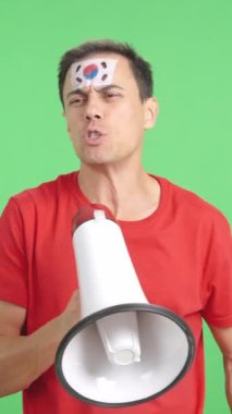 Stüdyoda, yüzünde Güney Kore bayrağı olan bir adamın kromasıyla kalabalığı megafonla canlandıran bir video.