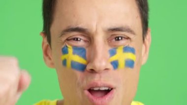 Stüdyoda, İsveçli bir adamın yüzü İsveç takımını destekleyen bir resminin krom görüntüsü var.