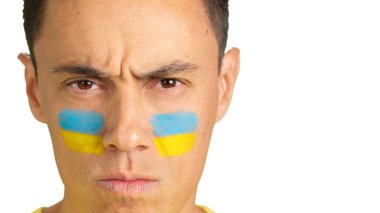 Yüzünde Ukrayna bayrağı olan ve kameraya bakan ciddi bir adamın yakın çekimi.