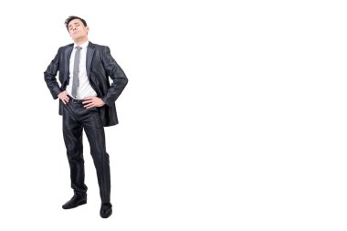 Resmi takım elbiseli kibirli bir adam elleri belinde kameraya bakıyor. Stüdyoda beyaz arka planda izole edilmiş.