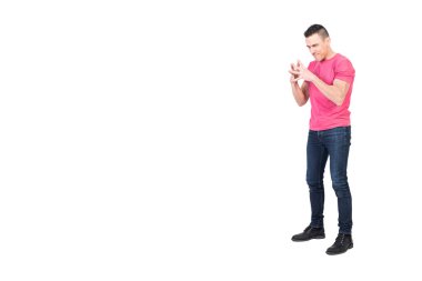 Uzun boylu, siyah saçlı, kot pantolonlu, parmaklarını birbirine bağlayan ve beyaz arka planda kameraya bakan kurnaz bir genç.