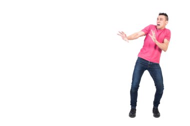 Kot pantolon ve pembe tişörtlü, uzun boylu, korkmuş bir erkek koruyucu jest yapıyor ve beyaz arka planda korku içinde bağırırken yüzünü çeviriyor.