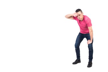 Uzun boylu, yorgun bir adam dizine yaslanıp alnından ter silerken beyaz arka planda kameraya bakıyor.