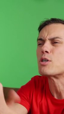 Evdeki kanepede oturan bir adam arkadaşlarıyla TV 'de maç izliyor. Ekibi bir şansı kaçırır ve umutsuzluğa kapılır. Yaklaş, kırmızı gömlek ve yeşil krom anahtar arka plan..