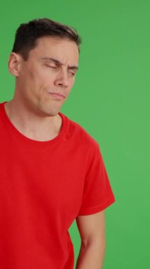 Yetişkin adam, yeşil ekranda izole edilmiş kopyalama alanını işaret eden tiksinti ve hoşnutsuzluk gösteren farklı yüzler yapıyor.