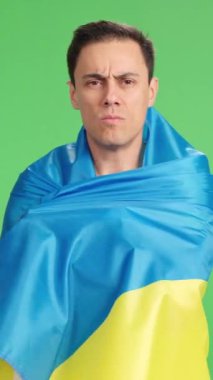 Ukrayna bayrağına sarılmış bir adam yeşil ekranda gururla kameraya bakıyor.
