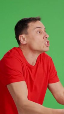 Kırmızı tişörtlü adam yeşil ekran arkaplanındaki fotokopi alanına bakan biriyle tartışıyor.