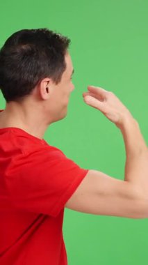 Kırmızı tişörtlü adam krom bir arka planda işaret ediyor, işaret ediyor ve gülümsüyor.