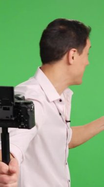 Yeşil ekran arkaplanı üzerine bir video blogu kaydederken çeşitli jestler yapan coşkulu içerik yaratıcısı