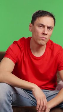 Evdeki kanepede üzgün ve bunalımda yatan bir adam film izlemeye çalışıyor ama canı bir şey yapmak istemiyor. Kırmızı tişört ve yeşil krom anahtar arka plan..