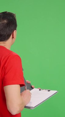 Arkası dönük teknisyen, yeşil ekran arkaplanındaki bir şeyi gözlemlerken panoya notlar alır.