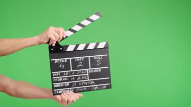 Film sayfası canlı yeşil bir ekrana karşı alkış tutuyor, bu da bir prodüksiyonun başladığını gösteriyor. Video düzenleme temaları ve film endüstrisi kavramları için mükemmel.