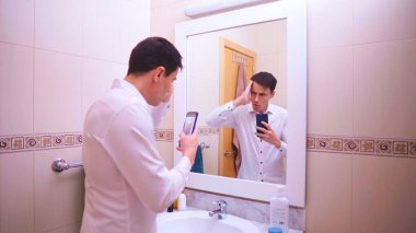 İşadamı banyo aynasında selfie çekiyor, en iyi pozu bulmaya çalışıyor.