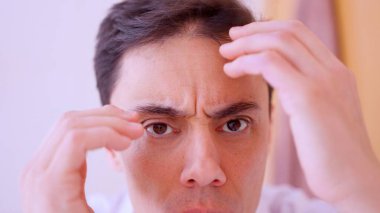 İş adamı saç dökülmesinden endişeleniyor, saç dökülmesi ve kellik belirtilerini kontrol ediyor.