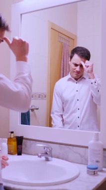 İş adamı endişeyle banyo aynası karşısında konuşma yapıyor ve gerginlik belirtileri gösteriyor.