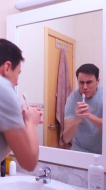 Adam mikrofon olarak diş fırçasını kullanıyor, banyo aynasında enerjik bir şekilde şarkı söylüyor, sabah rutininin tadını çıkarıyor.