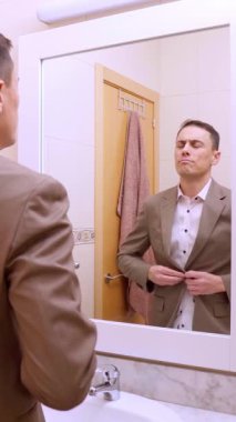 Takım elbisesini ayarlayan ve banyo aynasındaki yansımasına gülümseyen kendine güvenen bir iş adamı.
