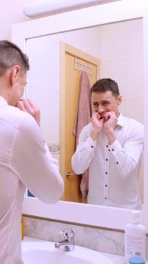 Banyodaki aynada dişlerini temizleyen ve kontrol eden bir iş adamı.