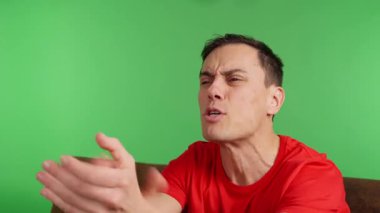 Evdeki kanepede oturan bir adam arkadaşlarıyla TV 'de maç izliyor. Ekibi bir şansı kaçırır ve umutsuzluğa kapılır. Yaklaş, kırmızı gömlek ve yeşil krom anahtar arka plan..