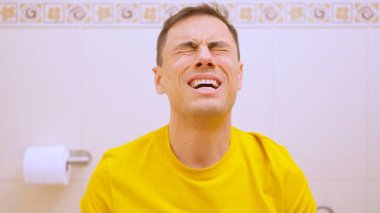 Adam tuvalette oturuyor ve kabızlık yüzünden çabalıyor.