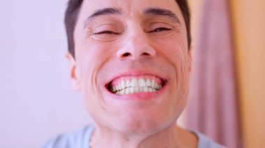 Adam dişlerini fırçaladıktan sonra banyoda dişlerini kontrol ediyor.