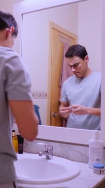 Genç adam banyo aynasının önünde kakao yağıyla dudaklarını nemlendiriyor.
