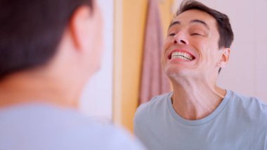 Adam dişlerini fırçaladıktan sonra banyo aynasında kusur arıyor.