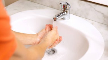 Adam banyo lavabosunda ellerini musluğun altında duruluyor.