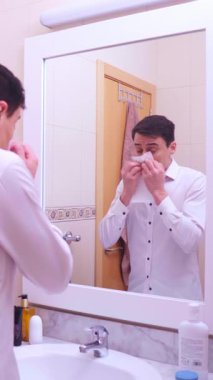 İş adamı aynaya bakıyor, burnunu siliyor ve mendilin içeriğinden korkuyor.