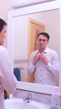 Ofis çalışanı gömleğinin düğmelerini iliklerken depresif bir ifadeyle aynada kendine bakıyor.