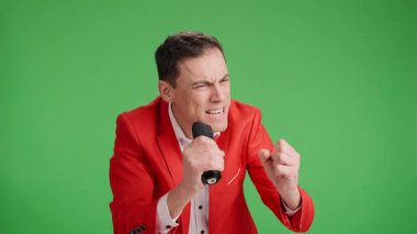 Enerjik şovmen, yeşil ekranda mikrofon kullanarak seyirciyi kendine çekiyor ve konserde sanatçıyı tanıtıyor.