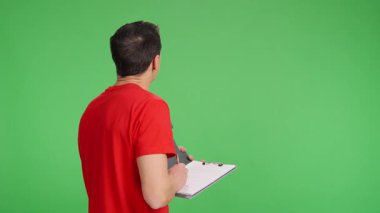Arkası dönük teknisyen, yeşil ekran arkaplanındaki bir şeyi gözlemlerken panoya notlar alır.