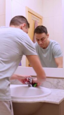 Sıradan kıyafetler giyen bir adam banyoyu ve musluğu dikkatlice temizliyor.